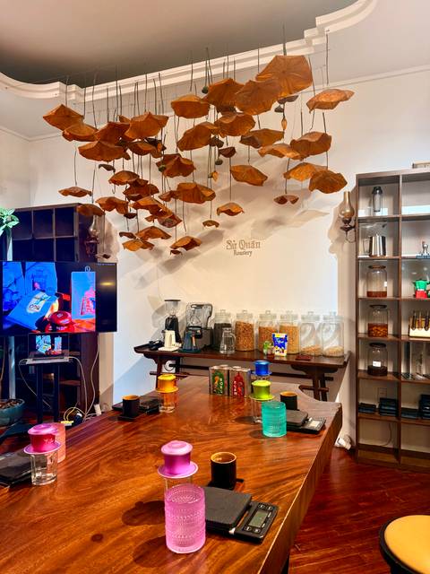       Stylish coffee workshop interior with hanging dried leaves and rows of beans, grinders and jars.
  