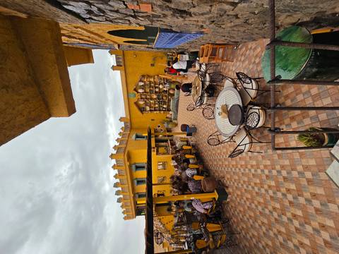       Colorful courtyard café with patterned tiles and yellow adobe walls bustling with guests.
  