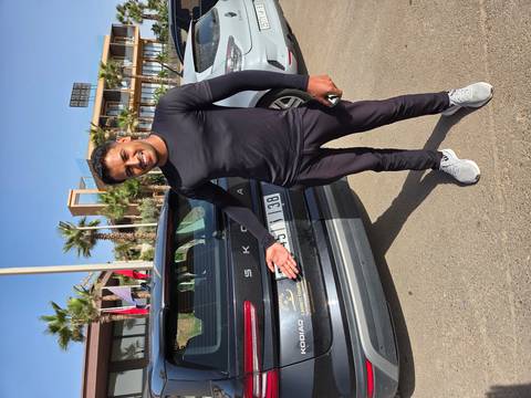       Smiling driver gestures toward a tour vehicle parked under clear blue sky.
  