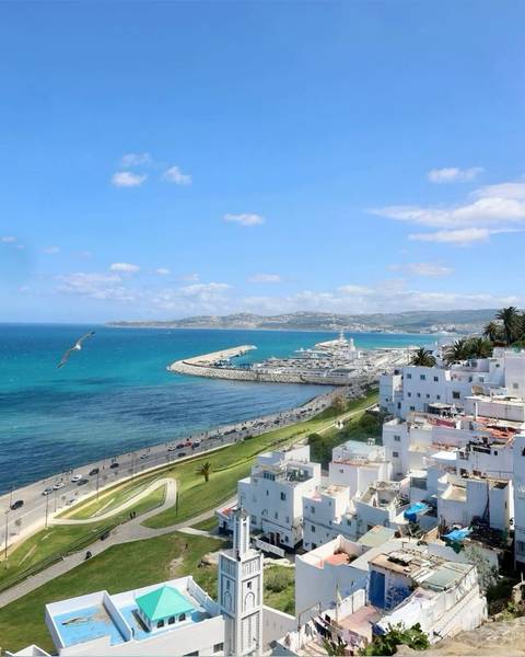       Bright coastal panorama of Tangier’s turquoise bay, harbour and white hillside homes under a clear sky.
  