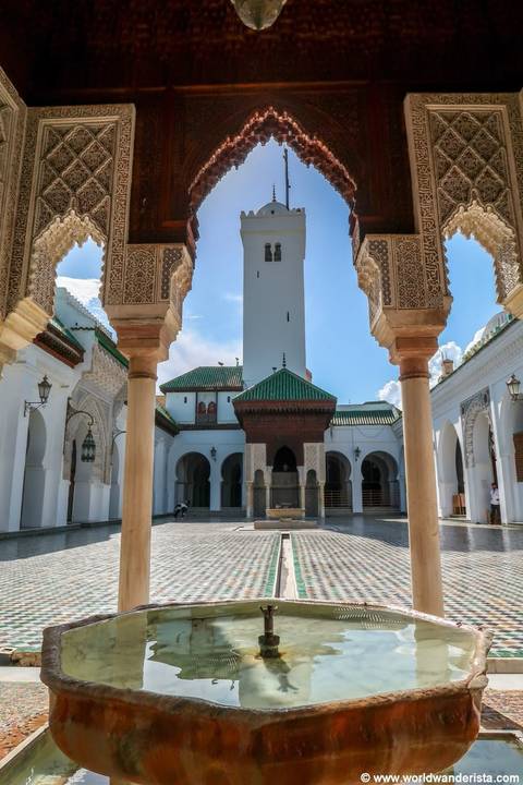       Ornate courtyard of a historic mosque with carved arches and a green-tiled roof, viewed through decorative columns.
  