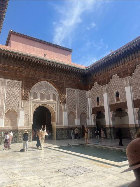       Intricately carved courtyard and archway of the Ben Youssef Madrasa with visitors admiring the historic interior.
  