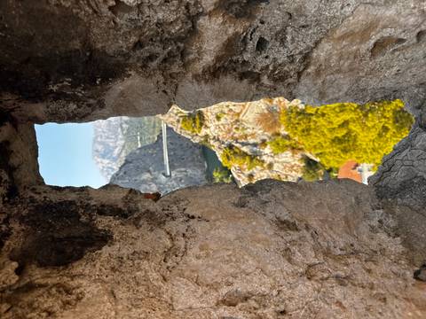       Rocky canyon and modern bridge seen through a narrow stone window slit of an old fortification.
  
