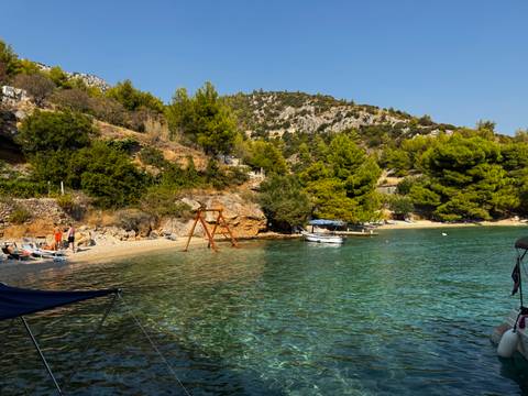       Secluded pebble beach with swing set, anchored boat and pine-covered hills around emerald water.
  