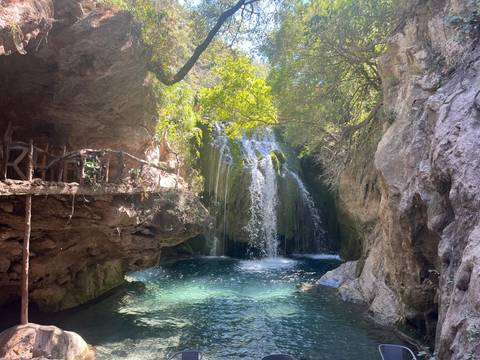      Clear turquoise pool and cascading waterfall shaded by lush greenery inside a rocky gorge.
  