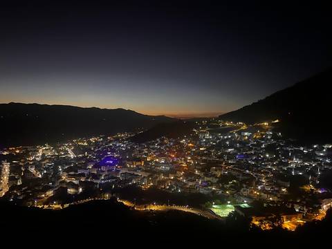       Elevated dusk view of a mountain town blanketed in twinkling lights under a fading sunset sky.
  