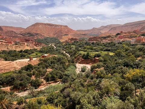       Lush green valley with scattered villages set against red-hued desert hills and distant mountains under a bright sky.
  