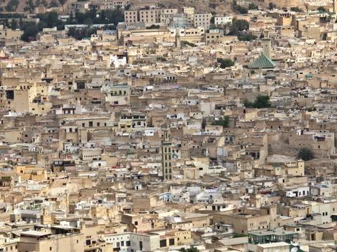       Dense beige rooftops of Fes’ ancient medina spread across the landscape with minarets peeking through.
  