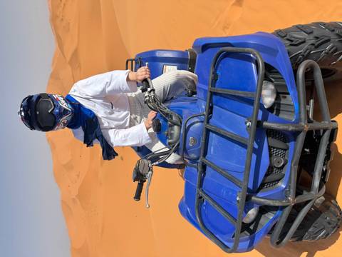      A rider wearing a blue scarf sits atop a blue quad bike ready to speed across the sand dunes.
  