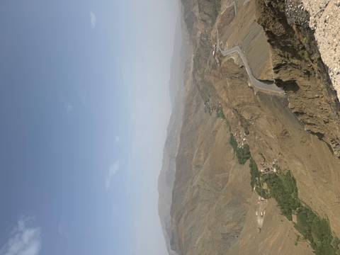       A distant mountain highway winds through rugged brown ridges toward a hazy horizon.
  