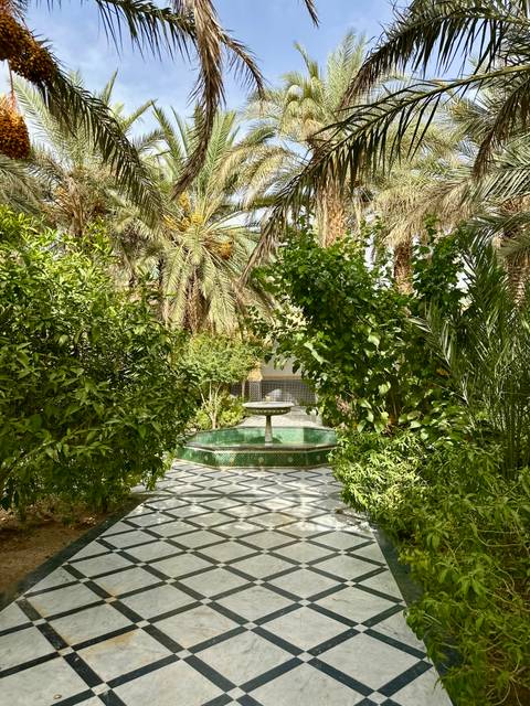       Lush riad garden with green tiled fountain surrounded by palms and citrus trees
  