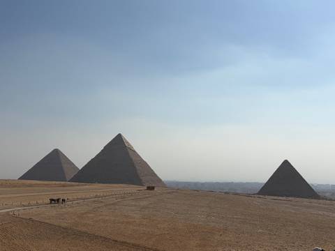       Iconic panorama of the three Great Pyramids rising from the desert plateau against a hazy sky.
  