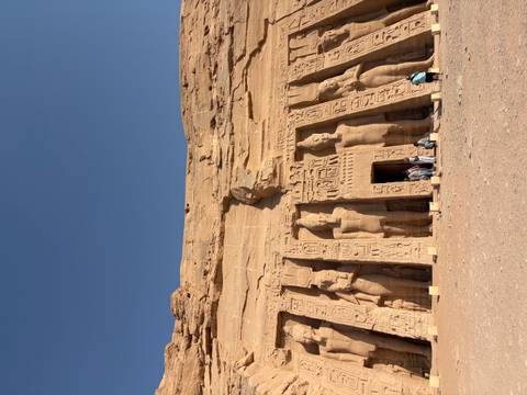       Visitors stand before the rock-cut Small Temple at Abu Simbel featuring colossal statues under a deep blue sky.
  