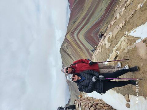       Two hikers posing on colorful striped slopes of Peru's Rainbow Mountain on cloudy day
  