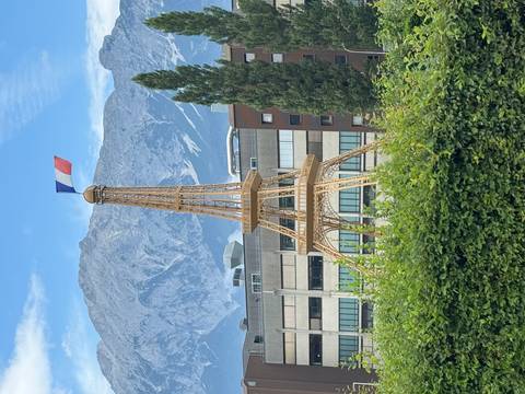       Small wooden replica of the Eiffel Tower with a French flag set in front of alpine mountains and offices
  