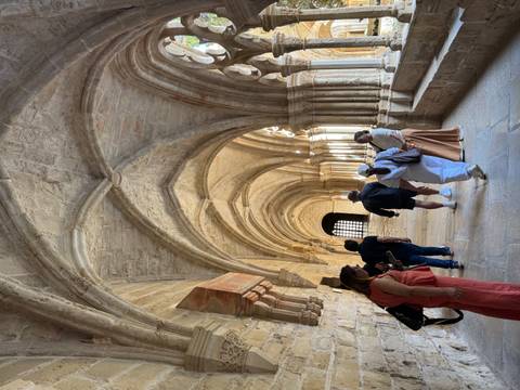       Visitors exploring a stone Gothic cloister with vaulted ceilings and warm lighting
  
