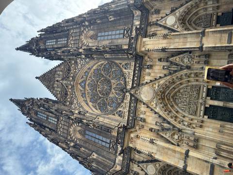       Gothic facade of St. Vitus Cathedral with intricate rose window, visitor photographing
  
