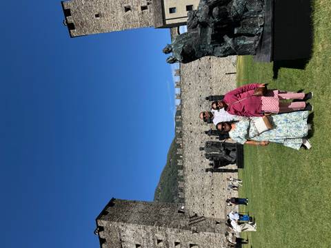       Family posing on lawn beside medieval stone walls and sculptures under blue sky
  