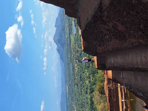      Hiker stands on ancient stone steps overlooking vast green plains and distant mountains from a high rock fortress.
  