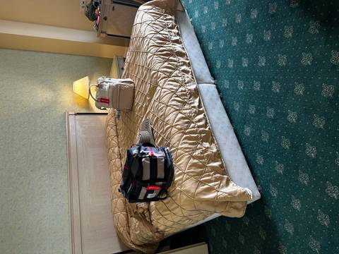       Hotel bedroom with personal luggage and hat placed on a quilted bedspread.
  