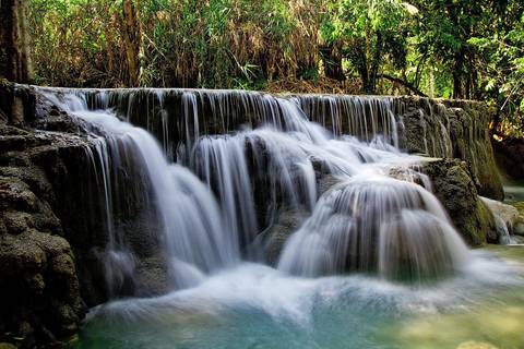       Silky turquoise cascades of Kuang Si Waterfall spilling over limestone tiers amid lush forest.
  