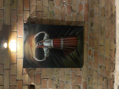       Painting of a hooded figure with scythes displayed on an exposed brick wall under a spotlight.
  