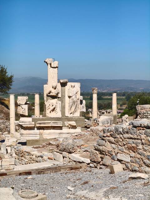       Ancient marble columns and reliefs of Ephesus rise against a clear blue Anatolian sky.
  