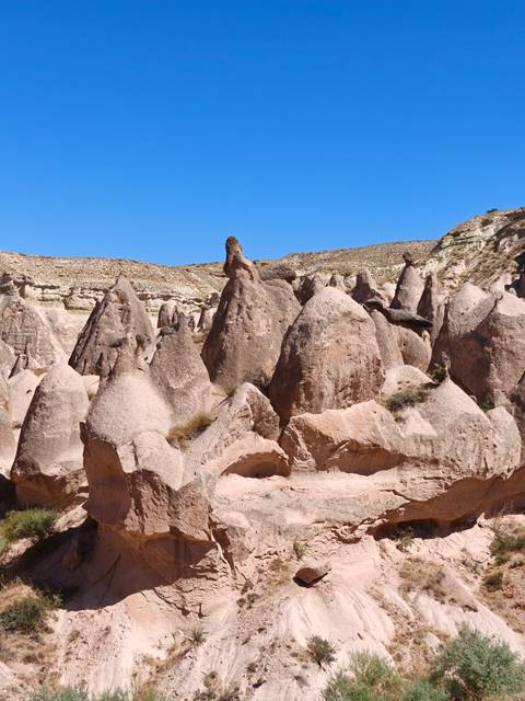       Pink-tinted rock pinnacles and fairy chimneys rise sharply against a clear Cappadocia sky.
  