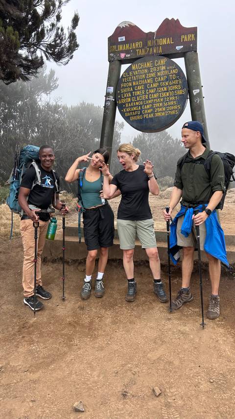       Trekking friends make playful faces with trekking poles amidst misty Kilimanjaro forest.
  