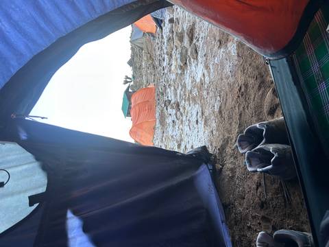       View out of a tent onto a rocky alpine campsite with orange tents and hiking boots in the foreground
  