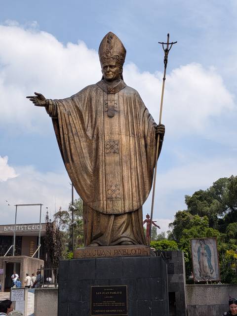       Tall bronze statue of a robed religious figure holding a staff against the sky
  