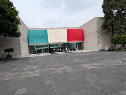       Entrance of museum draped with a massive Mexican flag over a stone façade
  