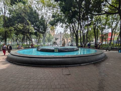       Circular fountain with playful statues in a shaded city park plaza
  
