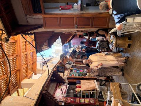       Bustling covered alley in the Fes medina with locals in traditional dress, colorful goods and carved wooden ceilings.
  