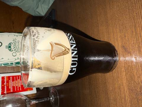       Pint glass of dark Guinness stout on a pub table with branded logo and creamy head.
  