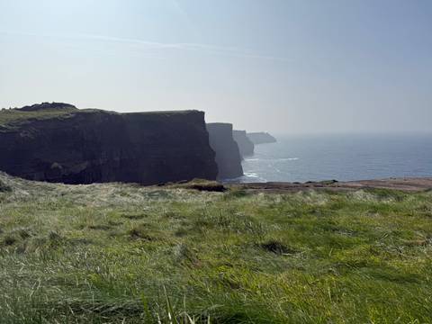       Iconic sheer sea cliffs dropping into the Atlantic Ocean under a hazy blue sky.
  