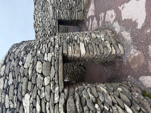       Ancient dry-stone beehive huts with narrow doorways and rough stone flooring under an overcast sky.
  