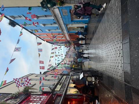       Lively pedestrian street lined with colorful buildings and overhead international flags after a light rain.
  