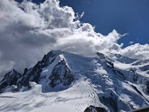       Dramatic snow-covered alpine peaks and glaciers piercing swirling clouds under a deep blue sky.
  