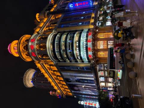       Illuminated New World department store building on busy Nanjing Road at night with traffic and pedestrians
  