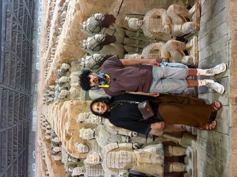       Two visitors posing in front of rows of terracotta warriors and horses inside the excavation pit
  