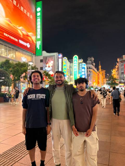       Three young men smiling together on neon-lit pedestrian street at night
  
