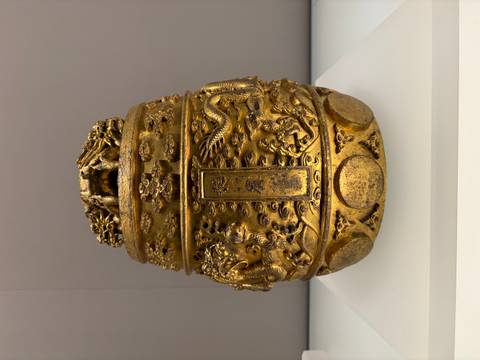      Close-up of an ornate golden Chinese ceremonial vessel with dragon motifs displayed in a museum case
  