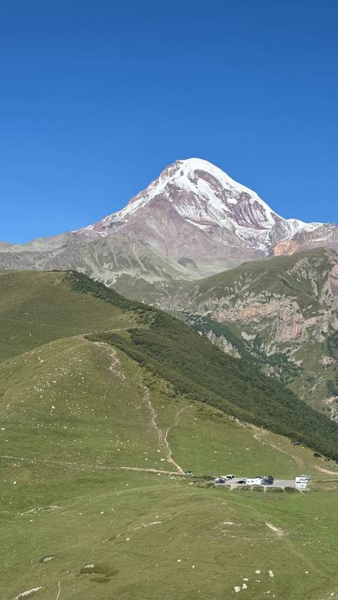       Snow-capped Mount Kazbek rising above rolling green ridges under a clear blue sky.
  