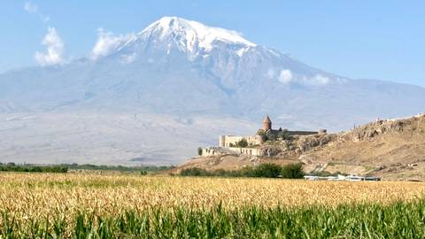       Golden cornfield leading to Khor Virap monastery with majestic snow-capped Mount Ararat behind.
  