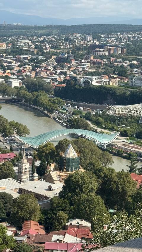       Aerial view of Tbilisi’s curving glass Bridge of Peace spanning the Kura River.
  