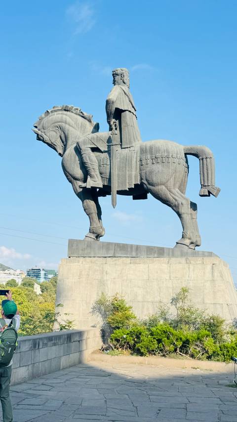       Stone equestrian statue of a medieval king against a clear blue sky.
  