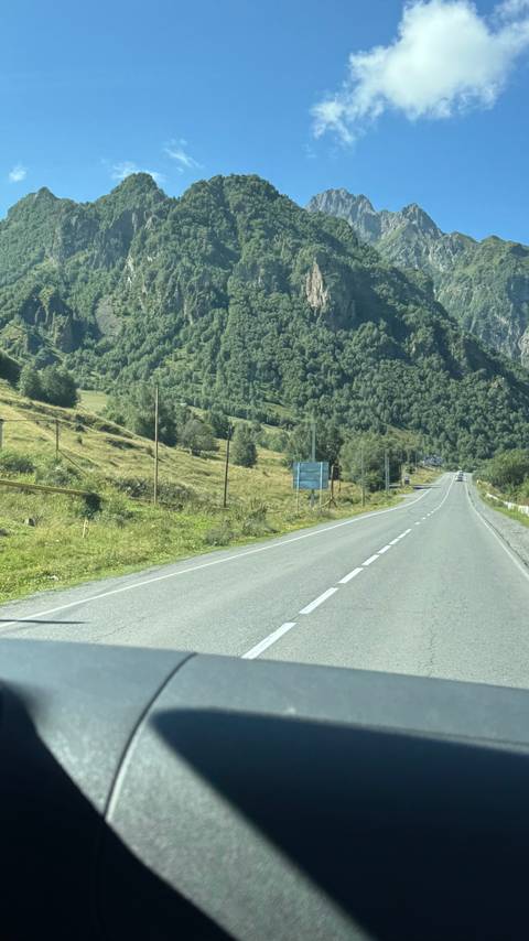       Empty country road winding through a lush green mountain valley.
  