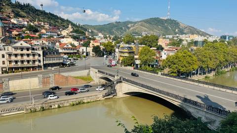       Panoramic view over the Kura River and Metekhi Bridge toward Tbilisi’s hillside neighborhoods.
  