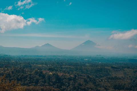       Hazy panoramic view of twin volcano peaks rising above a vast green valley under blue skies.
  